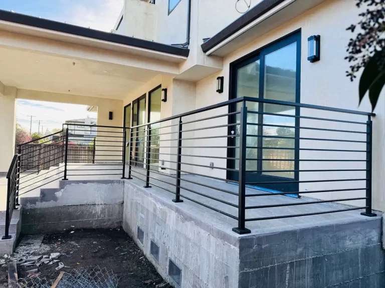 Residential deck with black metal railings and sliding glass doors in the background.