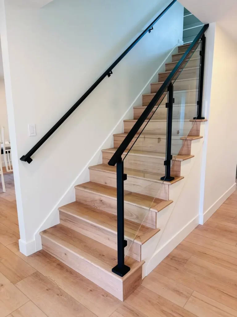 Downward view of staircase with glass railing and black handrail, showing the transition to the lower floor.