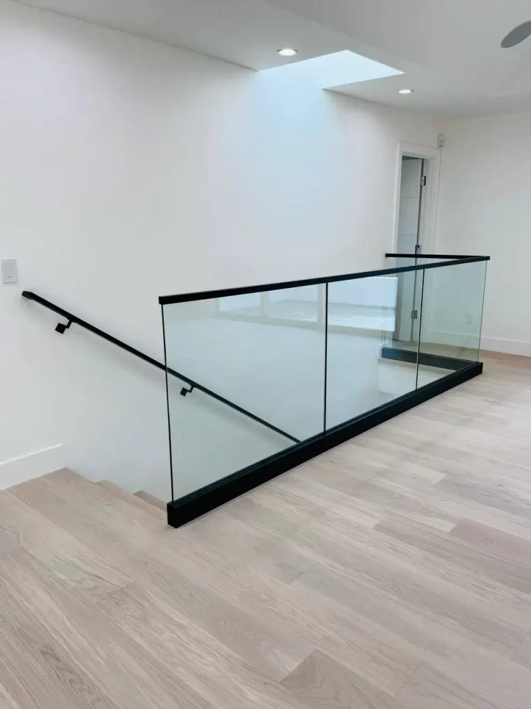 Close-up view of glass railing with black metal frame and wooden steps.