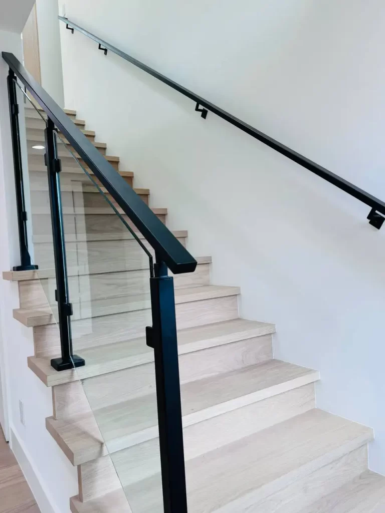 Interior staircase with tempered glass railing and black metal posts.