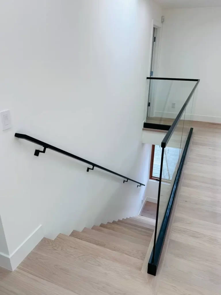 Top-down view of a staircase with a glass railing system, black handrail, and wooden steps.