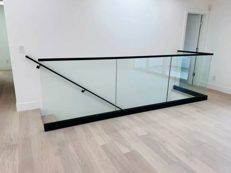 Modern glass railing with black trim, installed along a stairway and upper landing.